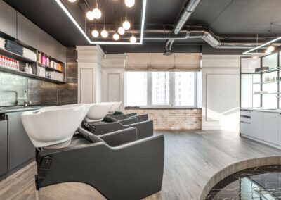 Black backwash chairs with sinks placed in modern spacious beauty salon with window and arrangement of cosmetology supply on shelves