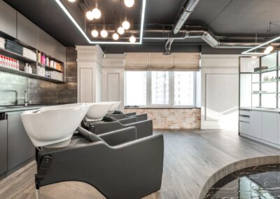 Black backwash chairs with sinks placed in modern spacious beauty salon with window and arrangement of cosmetology supply on shelves